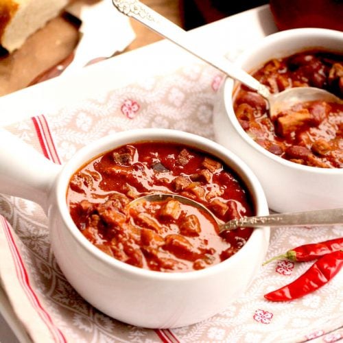 Venison Chili aka Deer Chili in white bowls with chili peppers on the side