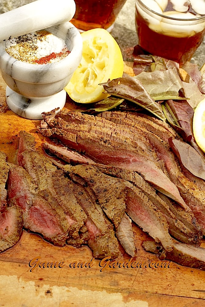 Tender venison hindquarter cuts with a garnish of lemons and greens, dusted with Perfect Dry Rub, with A cup of iced tea in the frame