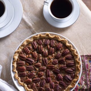 whole pecan pie in front of two cups of coffee in white china cups