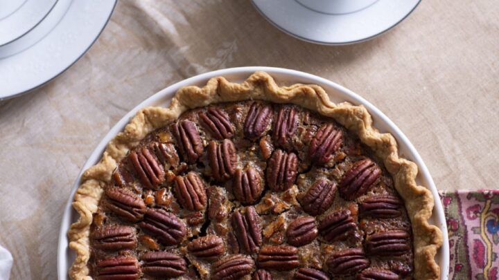 whole pecan pie in front of two cups of coffee in white china cups