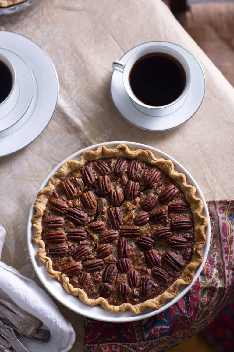whole pecan pie in front of two cups of coffee in white china cups