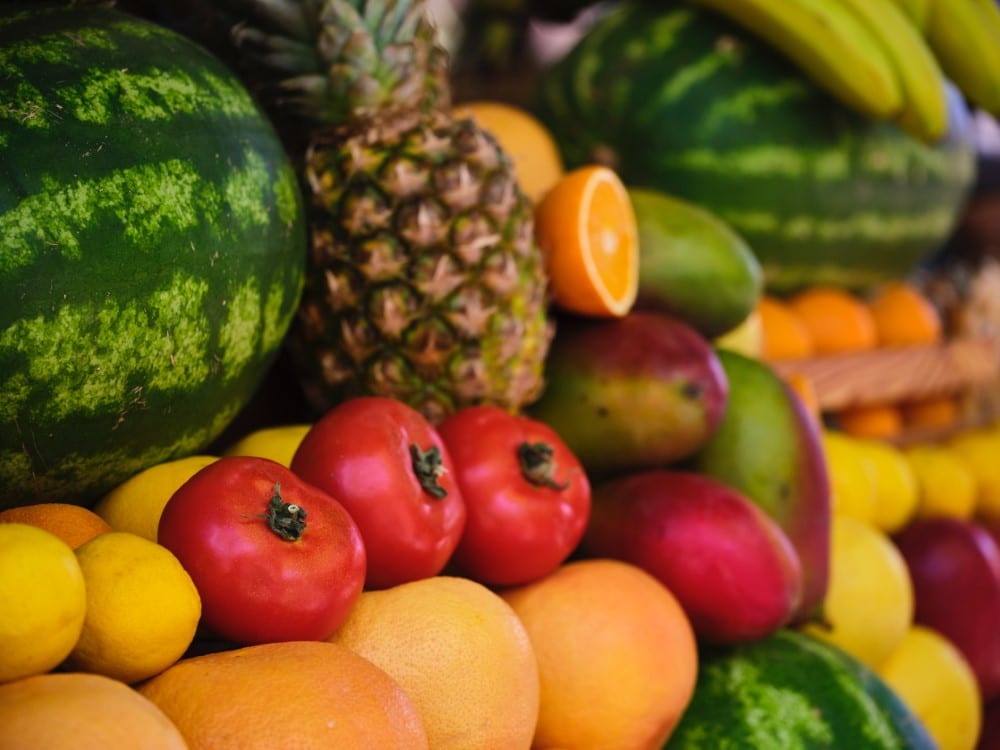 watermelon, tomatoes, mangos, pineapple, and other produce piled high at farmers' market