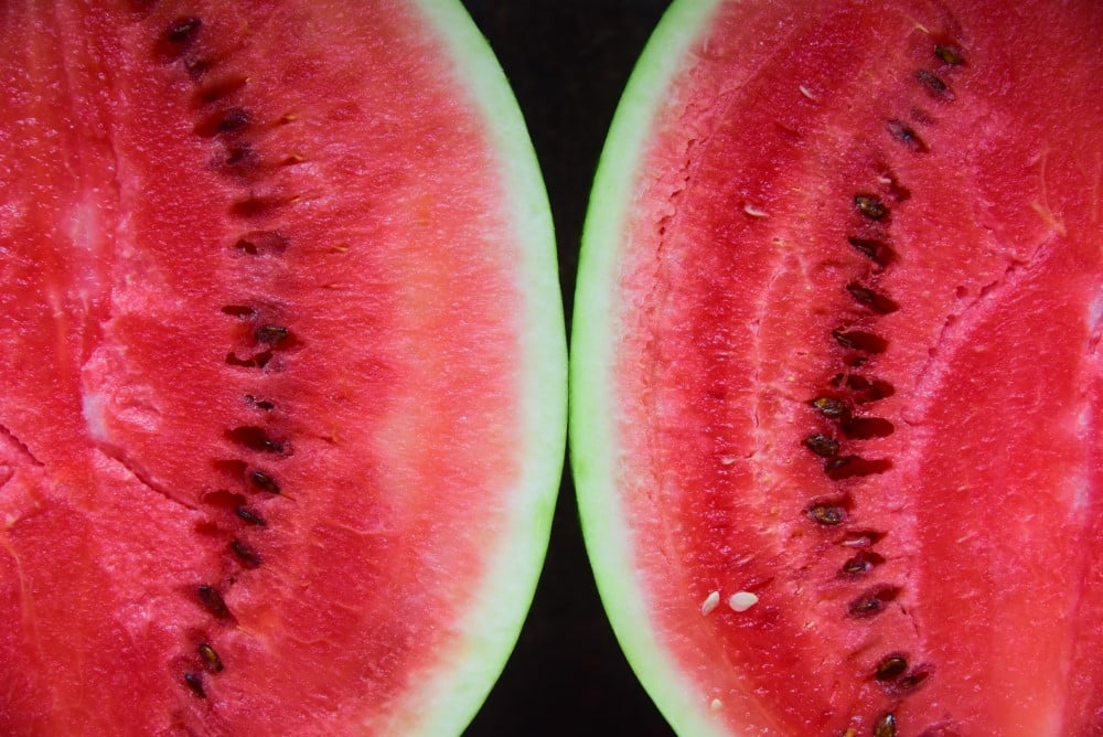 ripe watermelon sliced in half, closeup of red flesh and seeds
