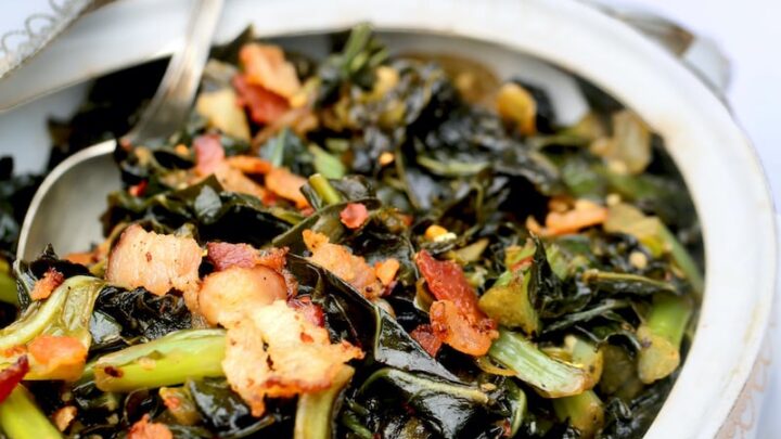 Collard greens with bacon on top in an antique white casserole dish with china plates in the background