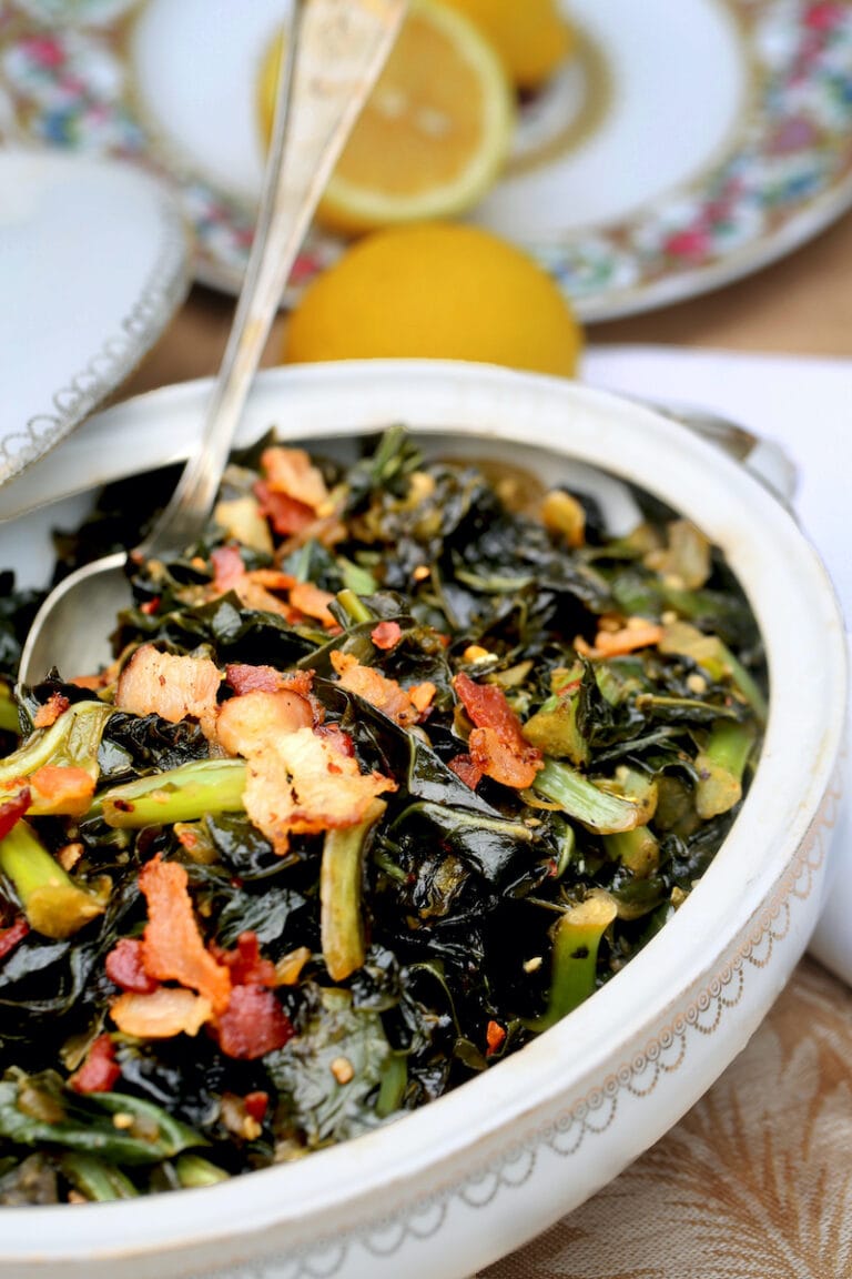 Collard greens with bacon on top in an antique white casserole dish with china plates in the background