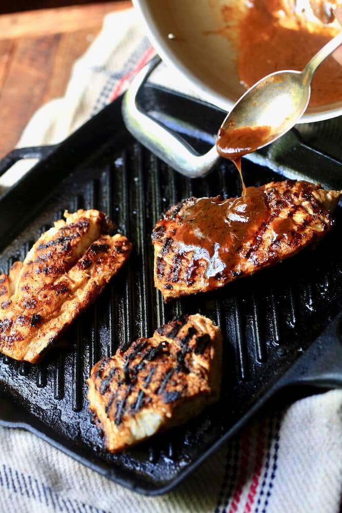 A picture of a spoon drizzling comeback sauce on Stacy Lyn Harris's seasoned Blackened Redfish dish