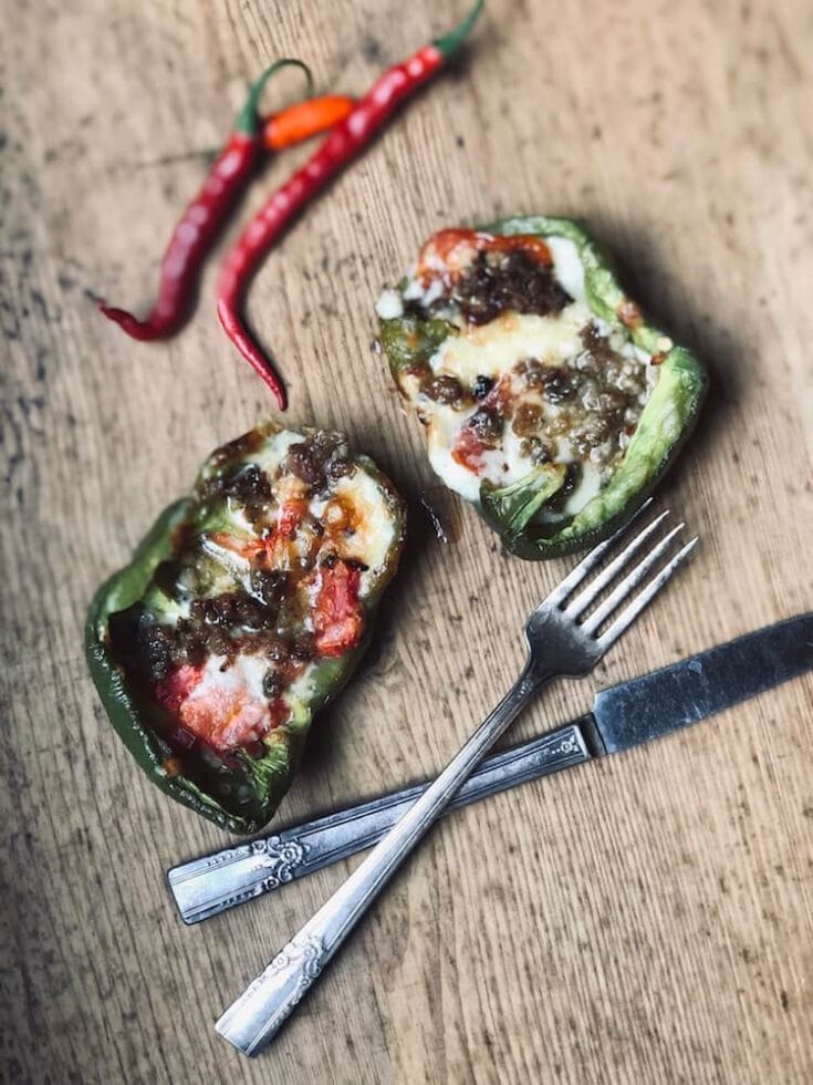 An image of Stacy Lyn Harris's Roasted Bell Peppers Stuffed with Sausage and Cheddar recipe, showing the bell peppers being stuffed with sausage and cheese