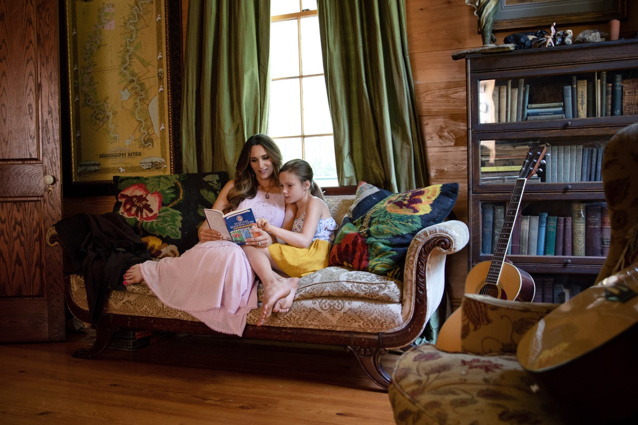 Stacy Lyn reading book to daughter on antique loveseat in family's living room