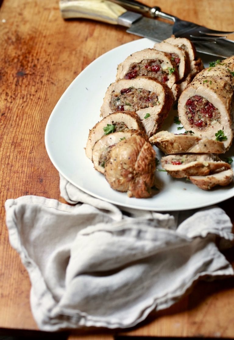Turkey Breast Stuffed with Sausage and Cranberries on a white plate on a wooden table with a linen napkin