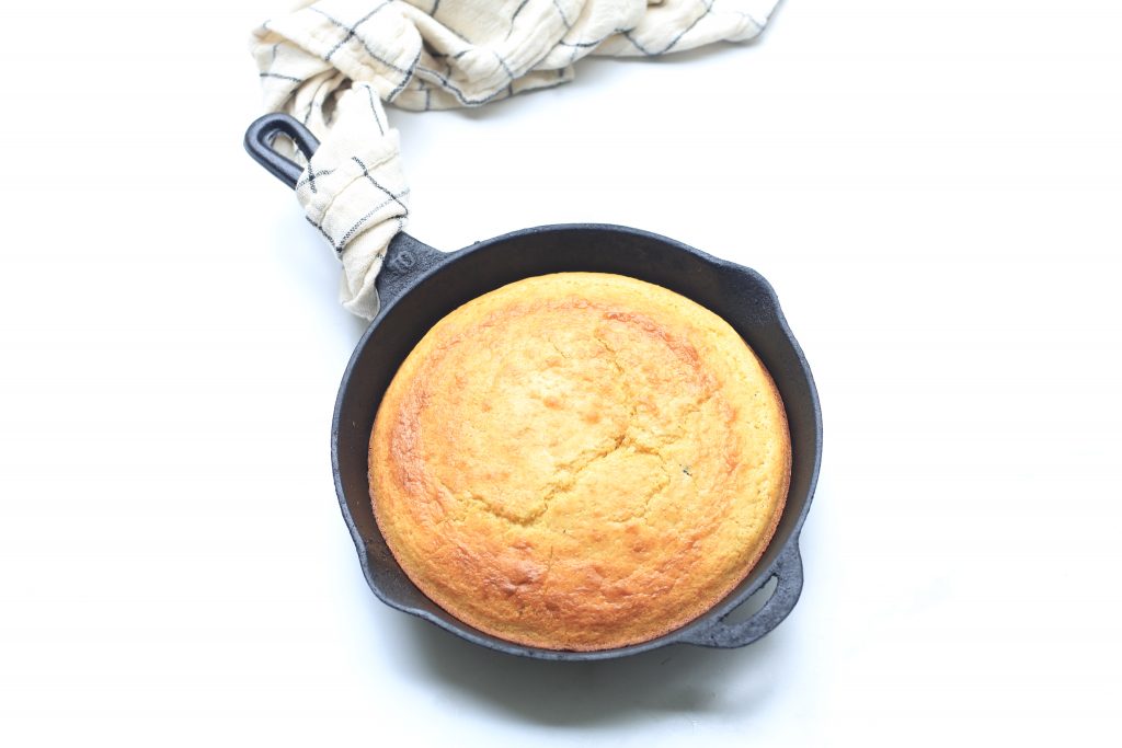 Cornbread in Black Skillet with Towel on White Background