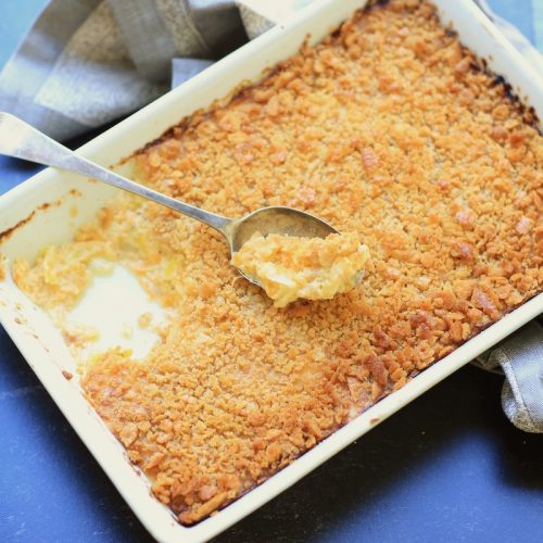 Squash casserole with ritz cracker topping in white rectangle pan over bright blue background