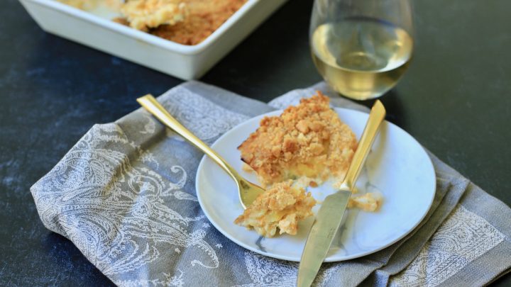 Squash casserole on a plate with fork with gray napkin under it with wine glass and casserole in background
