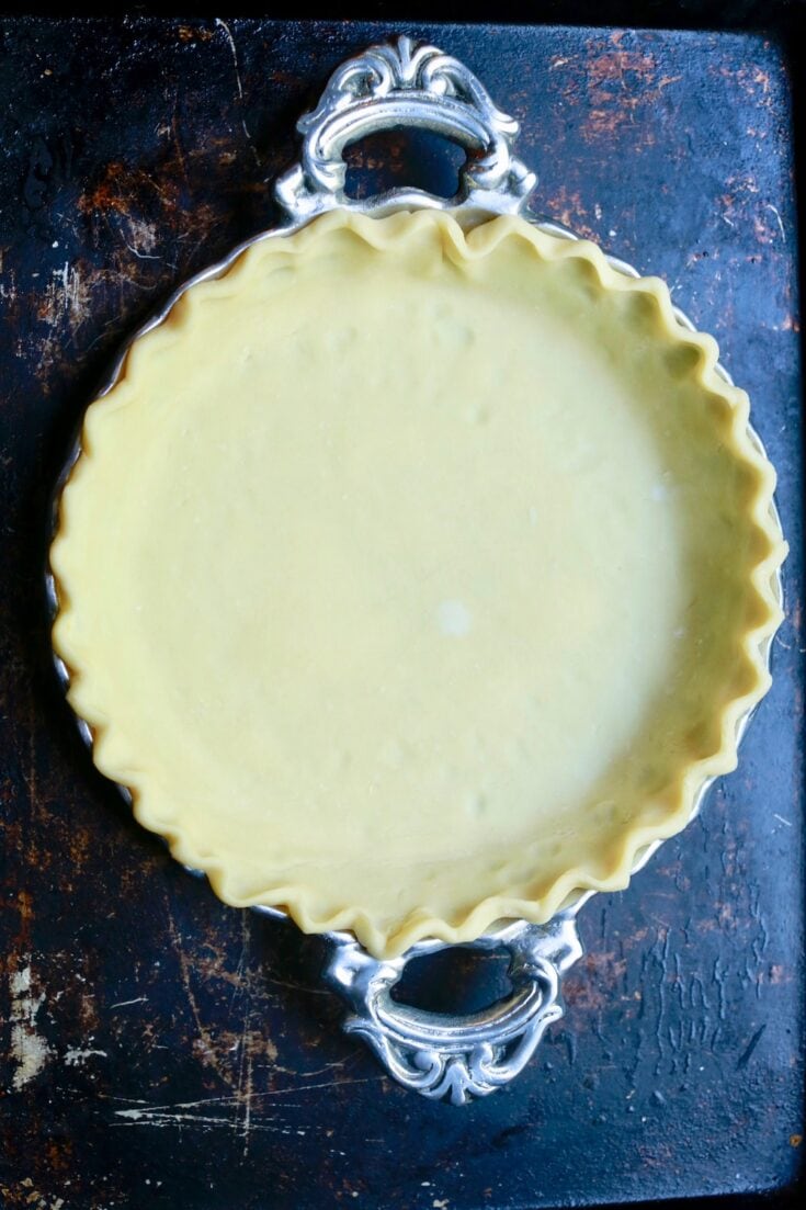 Pie dough in silver pie plate over black marble