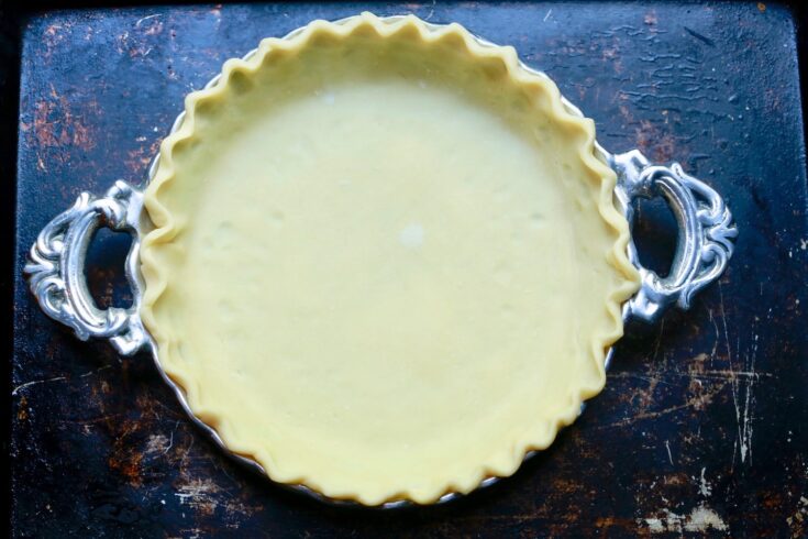 Homemade pie dough in silver pie plate on old baking sheet