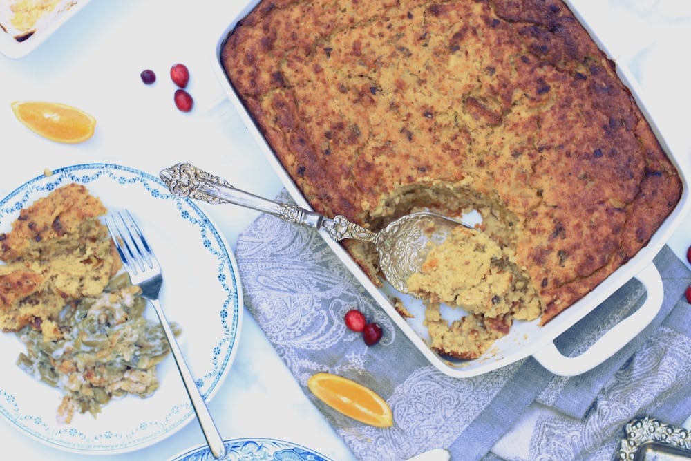Plate with sides for Thanksgiving on the left and dressing casserole on the right in large rectangle white casserole dish