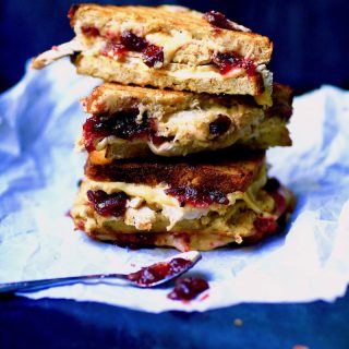 3 turkey and dressing sandwiches halved showing the cranberry sauce, melted cheeses on parchment paper with spoon having been in cranberry sauce