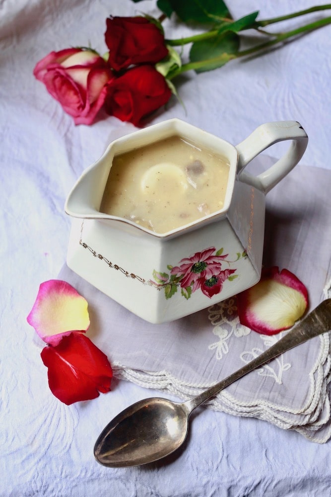 Giblet gravy in white serving dish on lavender table cloth with spoon in front of serving dish