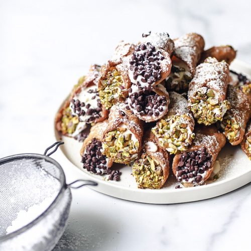 Canolli served on a white plate on white marble with chocolate and pistachio on the sides