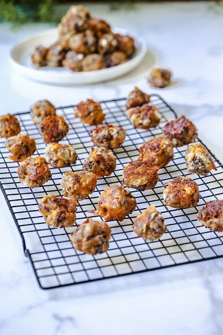 Sausage Balls on a cooling rack on white marble with a plate of sausage balls behind it.