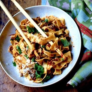Bolognese with Venison, Wild Boar, and Beef in a white bowl on wood surface with green napkin and chop sticks