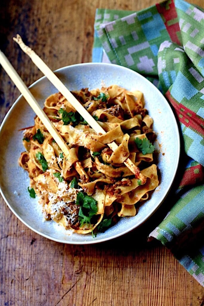 Bolognese with Venison, Wild Boar, and Beef in a white bowl on wood surface with green napkin and chop sticks