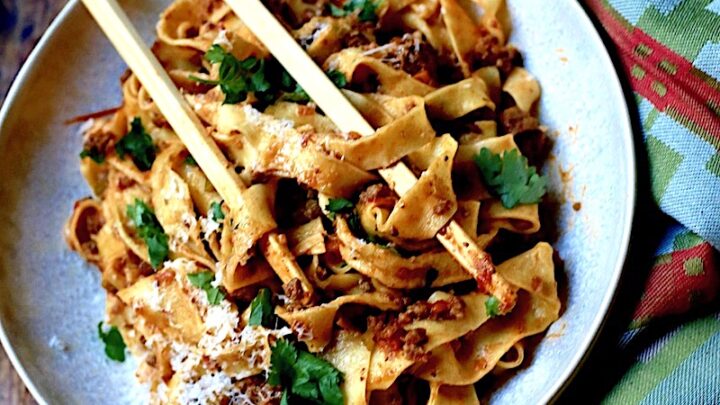 Bolognese with Venison, Wild Boar, and Beef in a white bowl on wood surface with green napkin and chop sticks