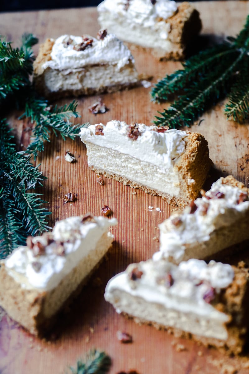 Eggnog Cheesecake with Candied Pecans placed sporadically on a board with Christmas Tree Limbs