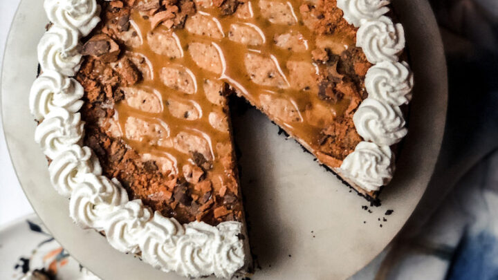 Top view of Butterfinger Cheesecake decorated with whipped cream around edges and plaid looking butterscotch drizzle