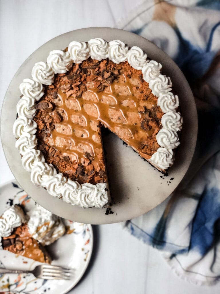 Top view of Butterfinger Cheesecake decorated with whipped cream around edges and plaid looking butterscotch drizzle
