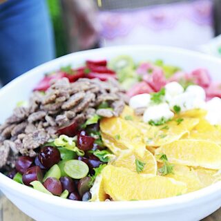 Salad in large white bowl filled with lettuce, pecans, orange slices, strawberries, grapes, strawberries, mozzarella on a table