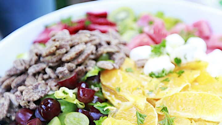 Salad in large white bowl filled with lettuce, pecans, orange slices, strawberries, grapes, strawberries, mozzarella on a table