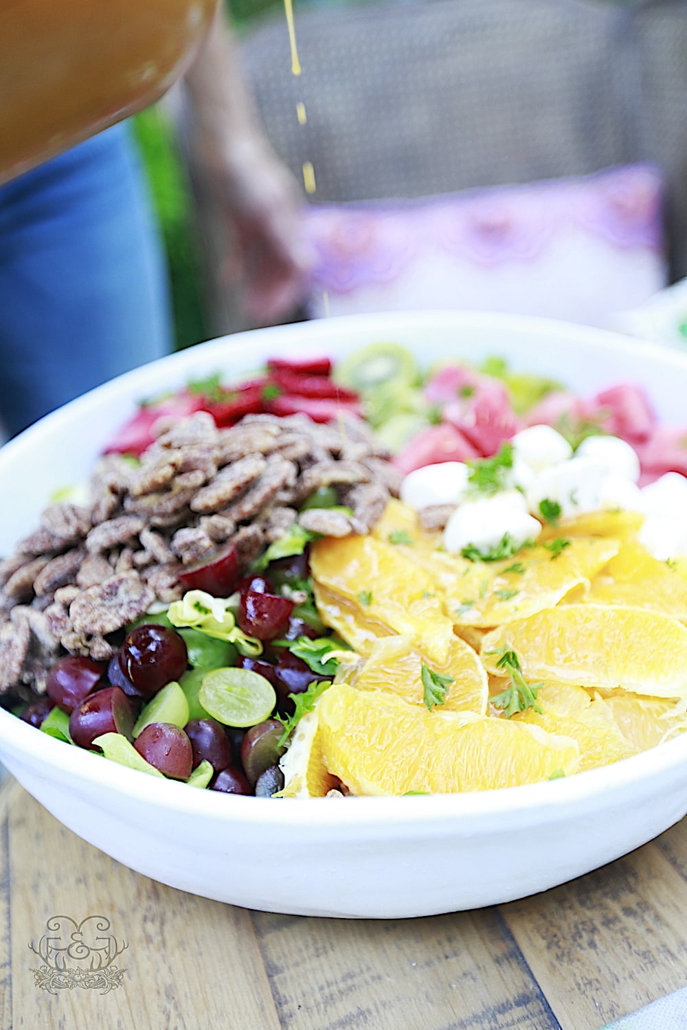 Salad in large white bowl filled with lettuce, pecans, orange slices, strawberries, grapes, strawberries, mozzarella on a table