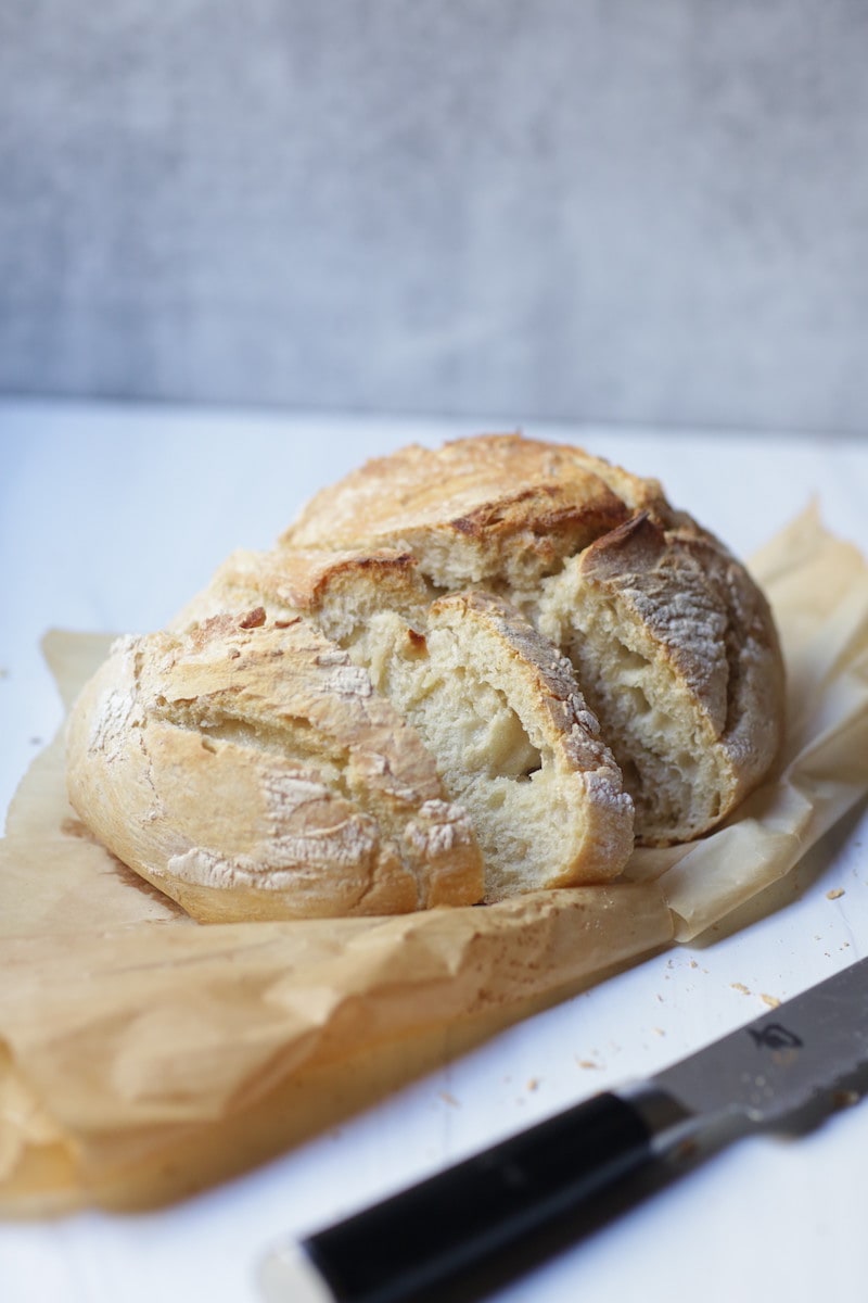 Artisan Bread on parchment with knife sitting beside it. on white and gray background.