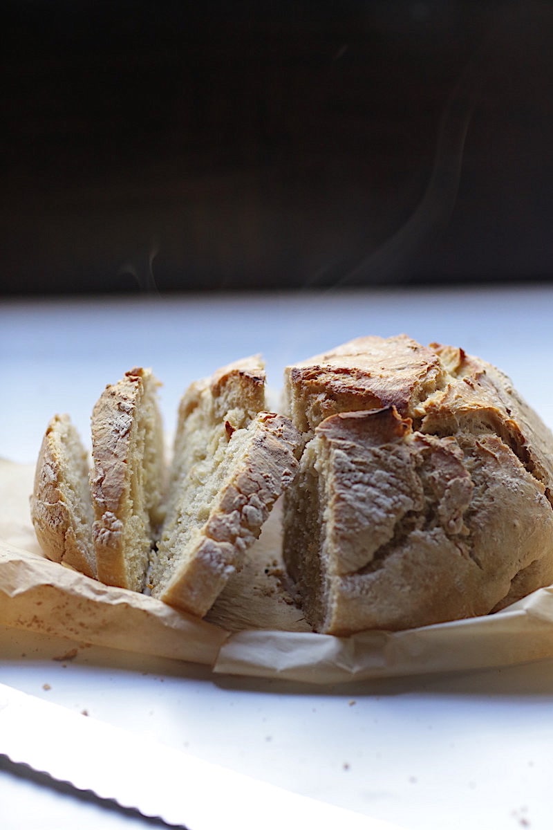 Artisan Crusty Bread on parchment paper on white background with black background with steam rising from the bread