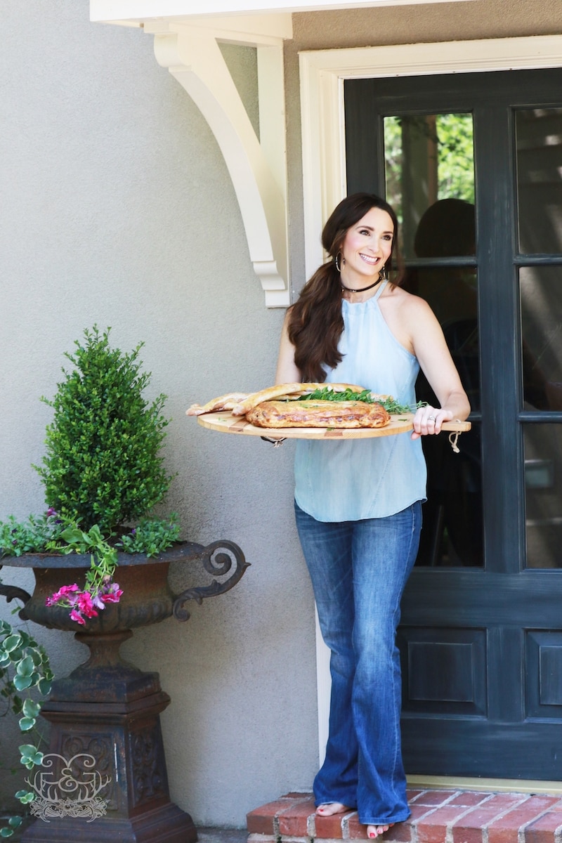 Stacy Lyn Harris holding a kale pastry on a cutting board in front of double doors barefoot