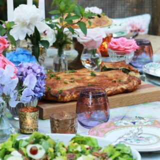 Outdoor party setting with table settings, flowers, glasses and kale pastry as centerpiece