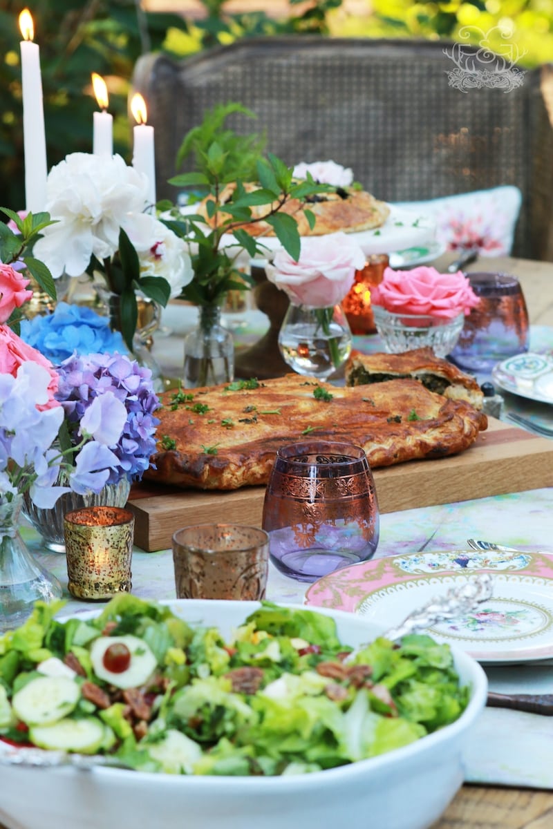 Outdoor party setting with table settings, flowers, glasses and kale pastry as centerpiece