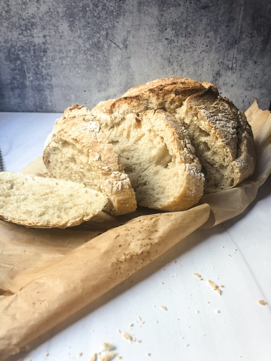 Crusty White bread on parchment paper on white surface with crumbs and gray background