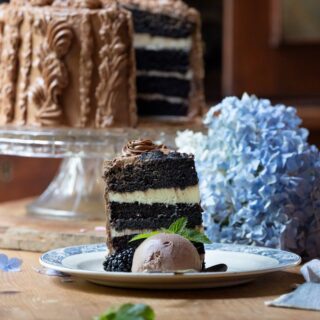 slice of beautiful cappuccino cake on wood table in front of the rest of the cake on cake stand