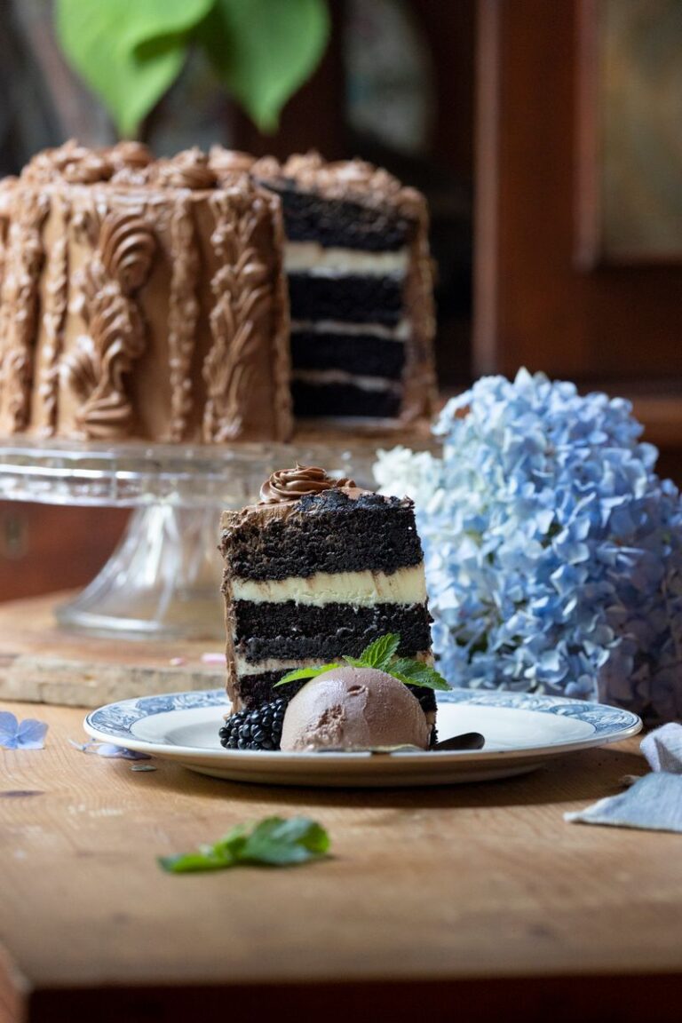 slice of beautiful cappuccino cake on wood table in front of the rest of the cake on cake stand