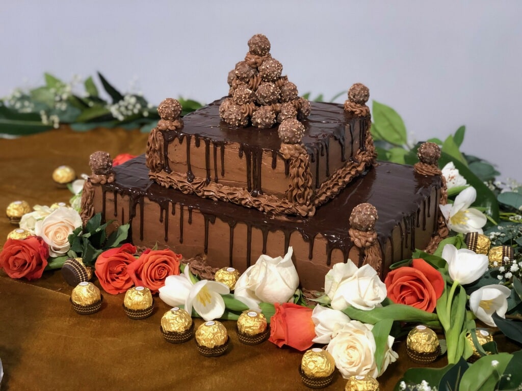 two-layer chocolate ganache groom's cake with chocolates on top and border of fresh red roses and white flowers