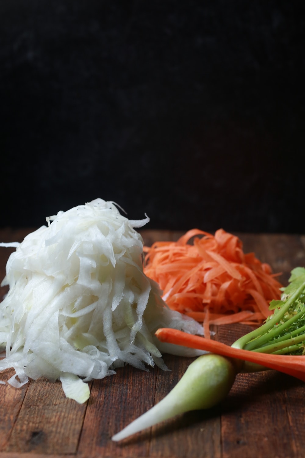 Peeled Daikon Radishes and Carrots on wood with a black background