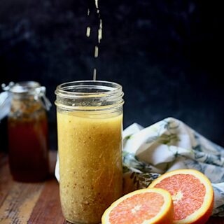Mason jar on wood with vinaigrette with black background with oranges and honey in the photo and red whisk