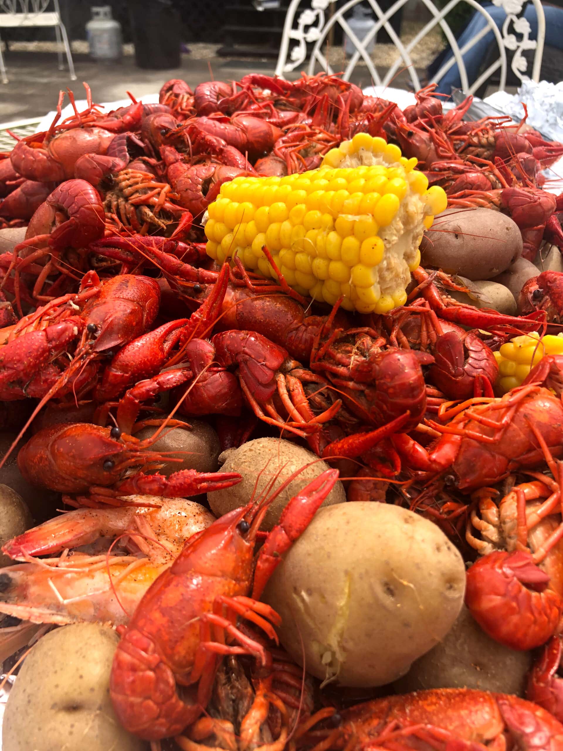 Bright Red Crawfish on a table with potatoes and a bright yellow corn with an outdoor chair