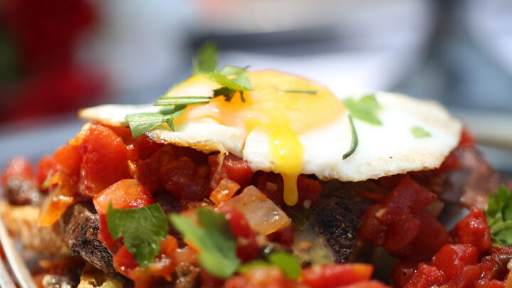 This fried egg sandwich is open faced with the egg atop tomato and venison or beef.
