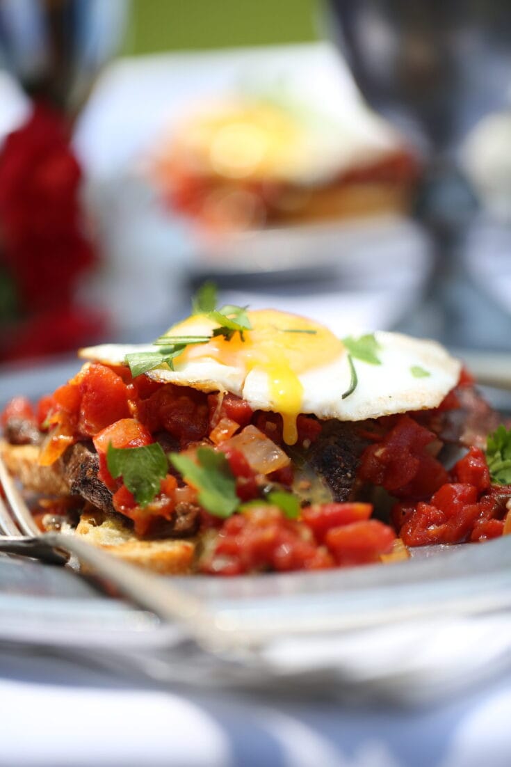 This fried egg sandwich is open faced with the egg atop tomato and venison or beef.