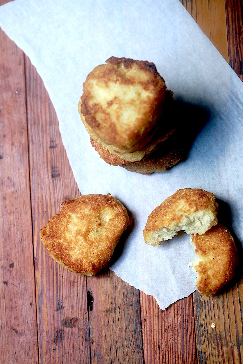 Overhead Fried Cornbread on Parchment, Some stacked and some laying on a board.