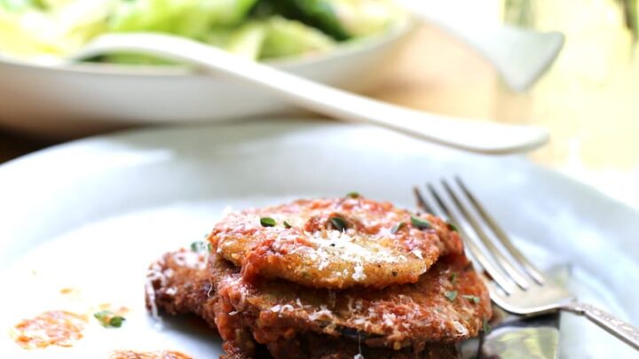 White Dish loaded with Venison Parmesan with tomato sauce and Parmesan cheese with salad in background
