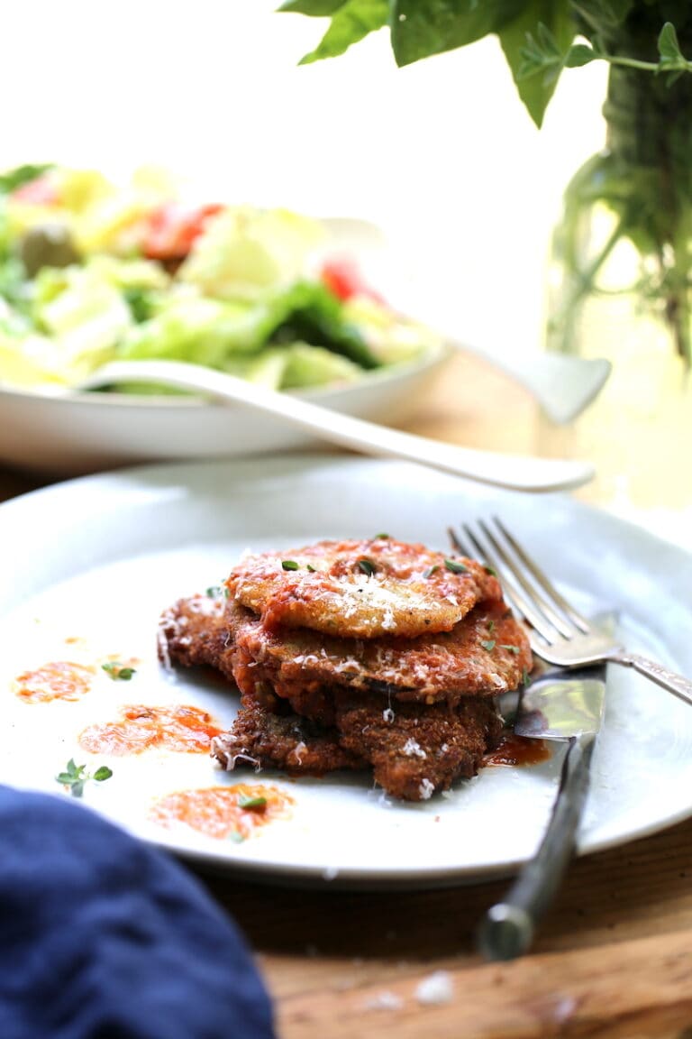 White Dish loaded with Venison Parmesan with tomato sauce and Parmesan cheese with salad in background