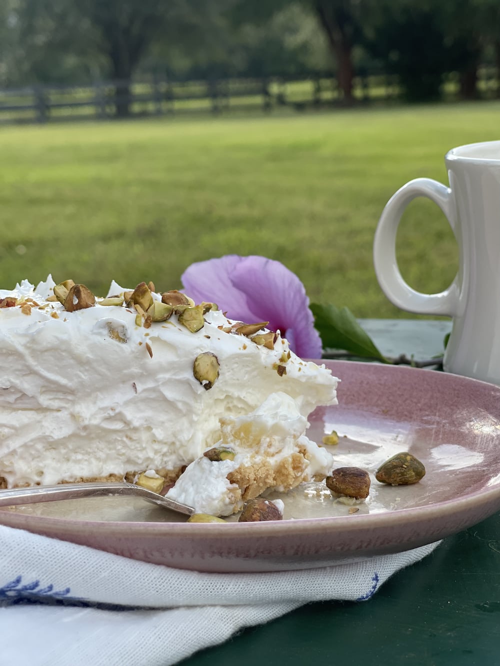Fork with Bite of Pineapple Pie on a Pink Plate with pie in background with pistachio nuts on top